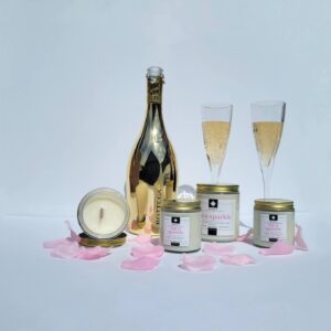 A collection of Alena’s Sip 'n Sparkle soy wax candles with gold lids and crackling wooden wicks. The elegant candles feature a soft glow, exuding hints of rose and sparkling notes, perfect for a luxurious ambiance.