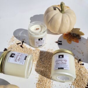 3 small pump up the chai Alena's candles on a white surface surrounded by pumpkins, leaves, and oats.