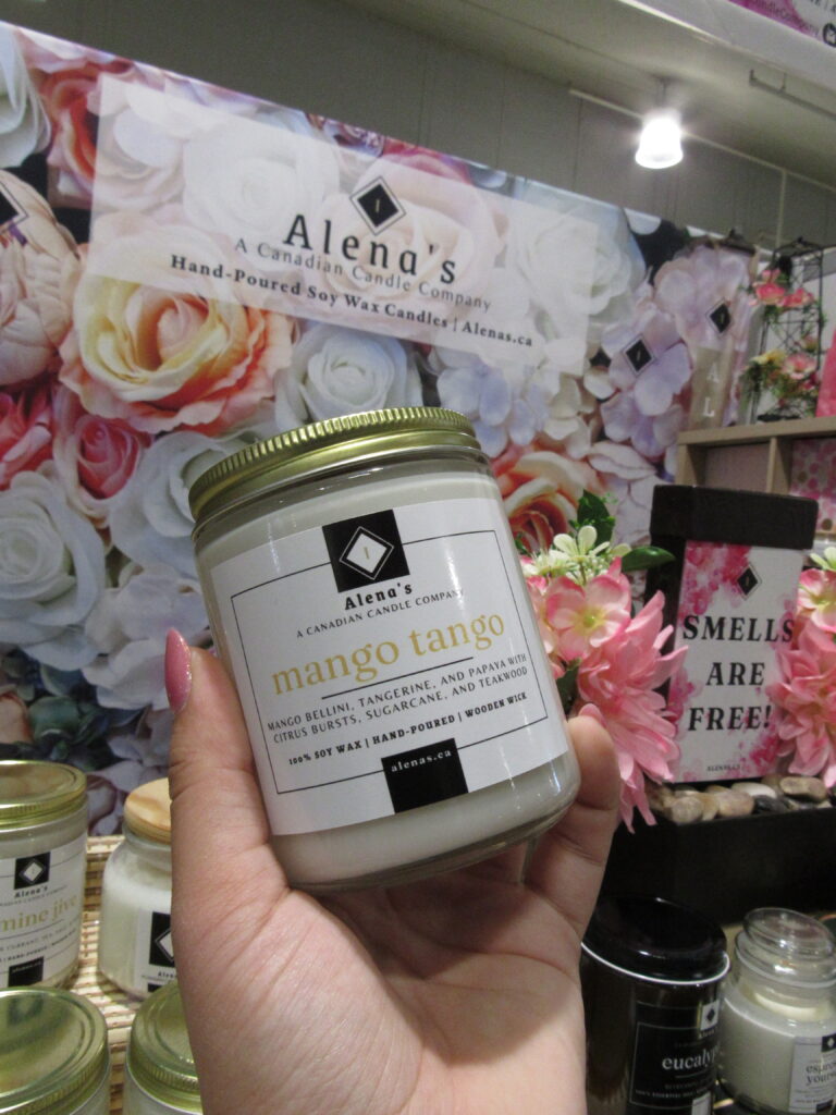 Mango Tango wooden wick soy wax candle in a clear glass jar, surrounded by fresh mango slices and tropical fruits. The candle glows warmly with a lit wooden wick, evoking a vibrant, fruity summer ambiance..