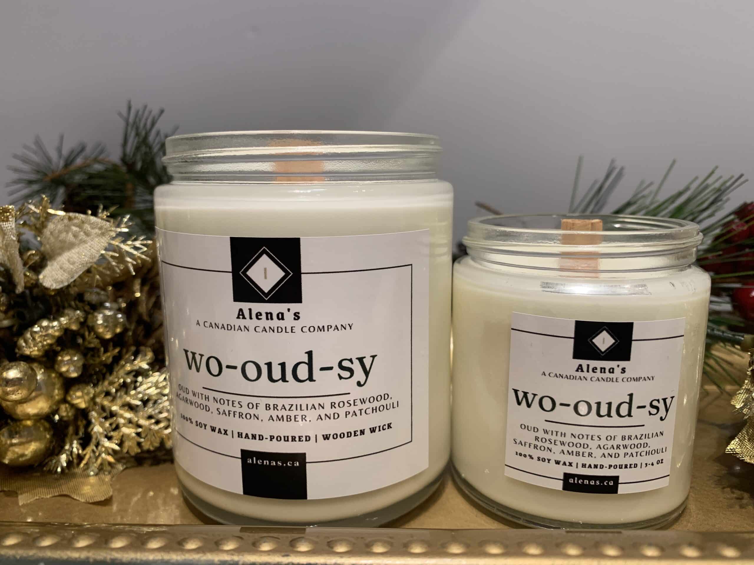 Wo-oud-sy 1 Alenas Wo- Oudsy Gold Lidded glass Jar Candles on a gold tray A rustic wooden candle jar labeled "Wo-oud-sy," surrounded by pieces of Brazilian rosewood, golden amber stones, and earthy foliage, evoking the warmth and richness of a summer bonfire.