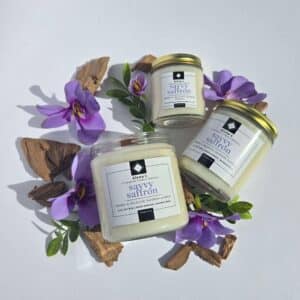 Savvy Saffron 16 oz flatlay candles on a whtie background surrounded by saffron flowers, wood pieces, and greenery