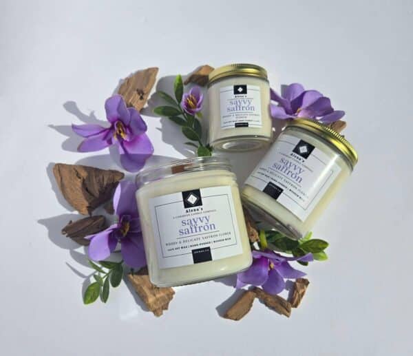Savvy Saffron 16 oz flatlay candles on a whtie background surrounded by saffron flowers, wood pieces, and greenery
