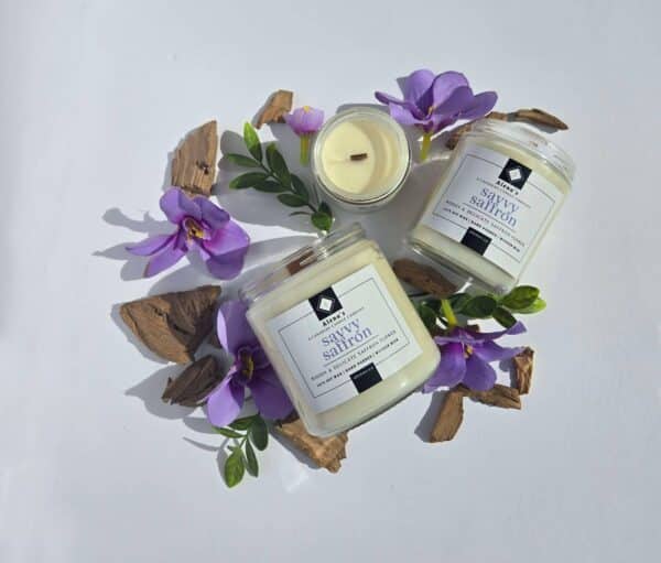 Savvy Saffron 16 oz flatlay candles on a whtie background surrounded by saffron flowers, wood pieces, and greenery