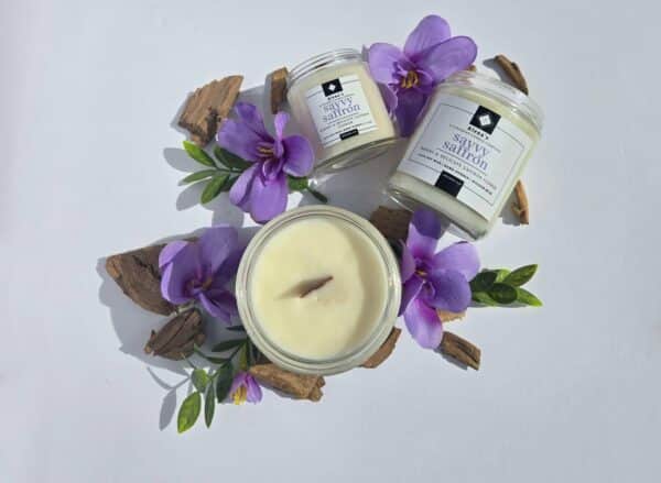 Savvy Saffron 16 oz flatlay candles on a whtie background surrounded by saffron flowers, wood pieces, and greenery