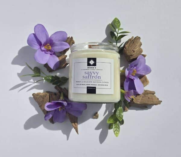Savvy Saffron 16 oz flatlay candle on a whtie background surrounded by saffron flowers, wood pieces, and greenery