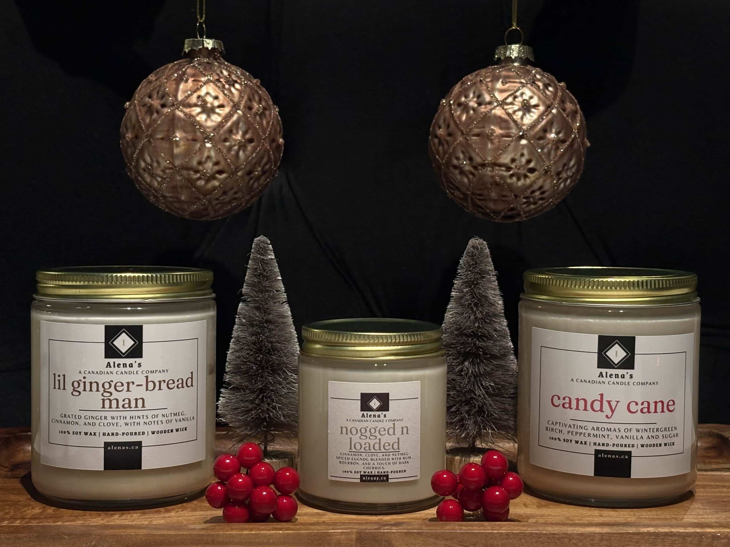 Alena’s Holiday Trio Candle Collection featuring Lil Gingerbread Man, Nogged N Loaded, and Candy Cane soy wax candles with wooden wicks in festive gold tins.