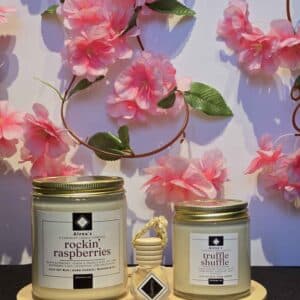 an 8 oz rockin raspberries, 4 oz truffle shuffle, a diffuser charm, on a wooden platform with cherry blossom flowers in the background