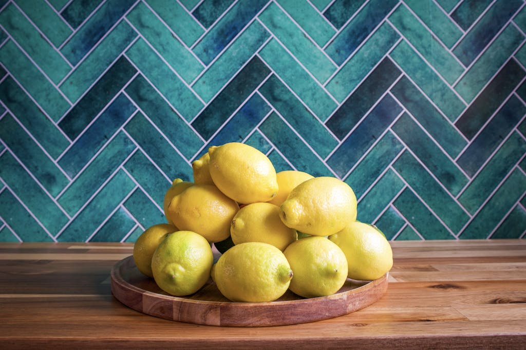 Customer Favourites — Start Here 25 A vibrant stack of lemons on a wooden tray with a teal chevron backdrop, perfect for decoration or healthy living themes.