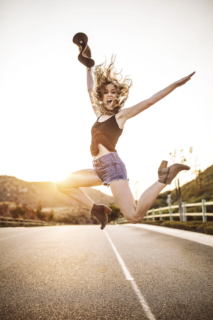 Happy woman jumping in the air on a sunny road with vibrant energy and joy.