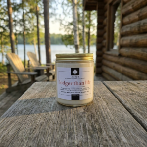 Alena’s Lodger Than Life soy candle in gold jar with view of lake and highback chairs at the cottage in Muskoka.