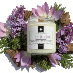 wooden wick candle on a white background with moss, cedar wood, lilacs, and waterlily petals surrounding it