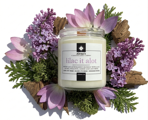 wooden wick candle on a white background with moss, cedar wood, lilacs, and waterlily petals surrounding it